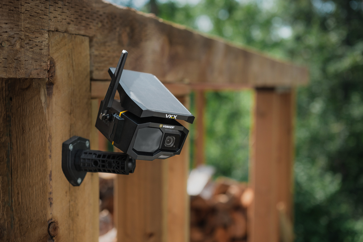 Outdoor security camera mounted on a wooden post with blurred greenery in the background